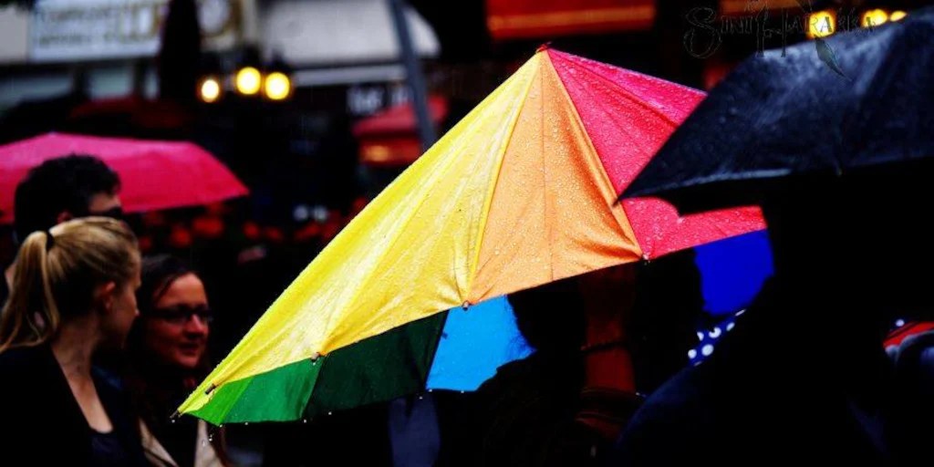 A large rainbow umbrella dominates two-thirds of the picture. 